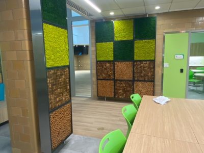 Modern office space with green chairs, wooden table, and decorative wall panels featuring green and brown textured squares.